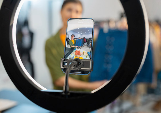Gravação de vídeo com celular em ring light dentro de uma loja, com a apresentadora ao fundo