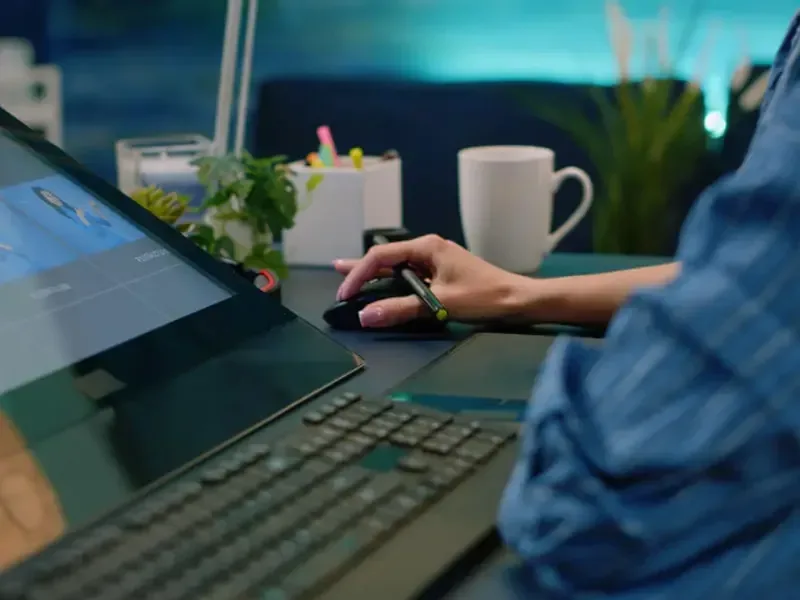 Pessoa trabalhando em computador com tablet e teclado na mesa, criando site para empresa